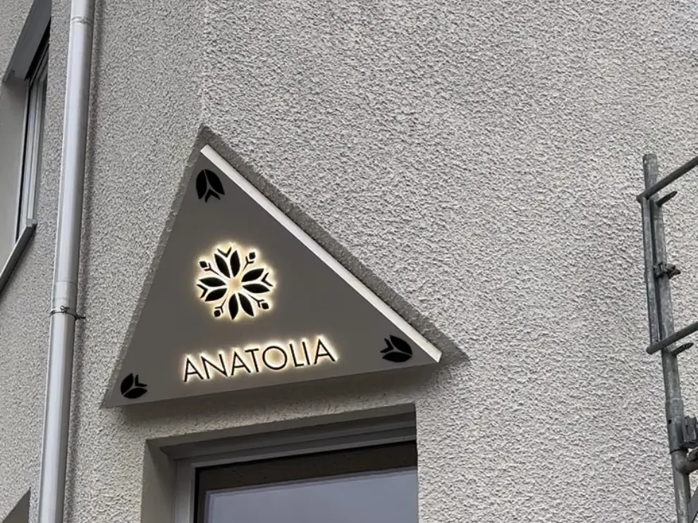 Dreieckiges Leuchtschild über einer Eingangstür mit hinterleuchteter Blüte und dem Schriftzug ANATOLIA