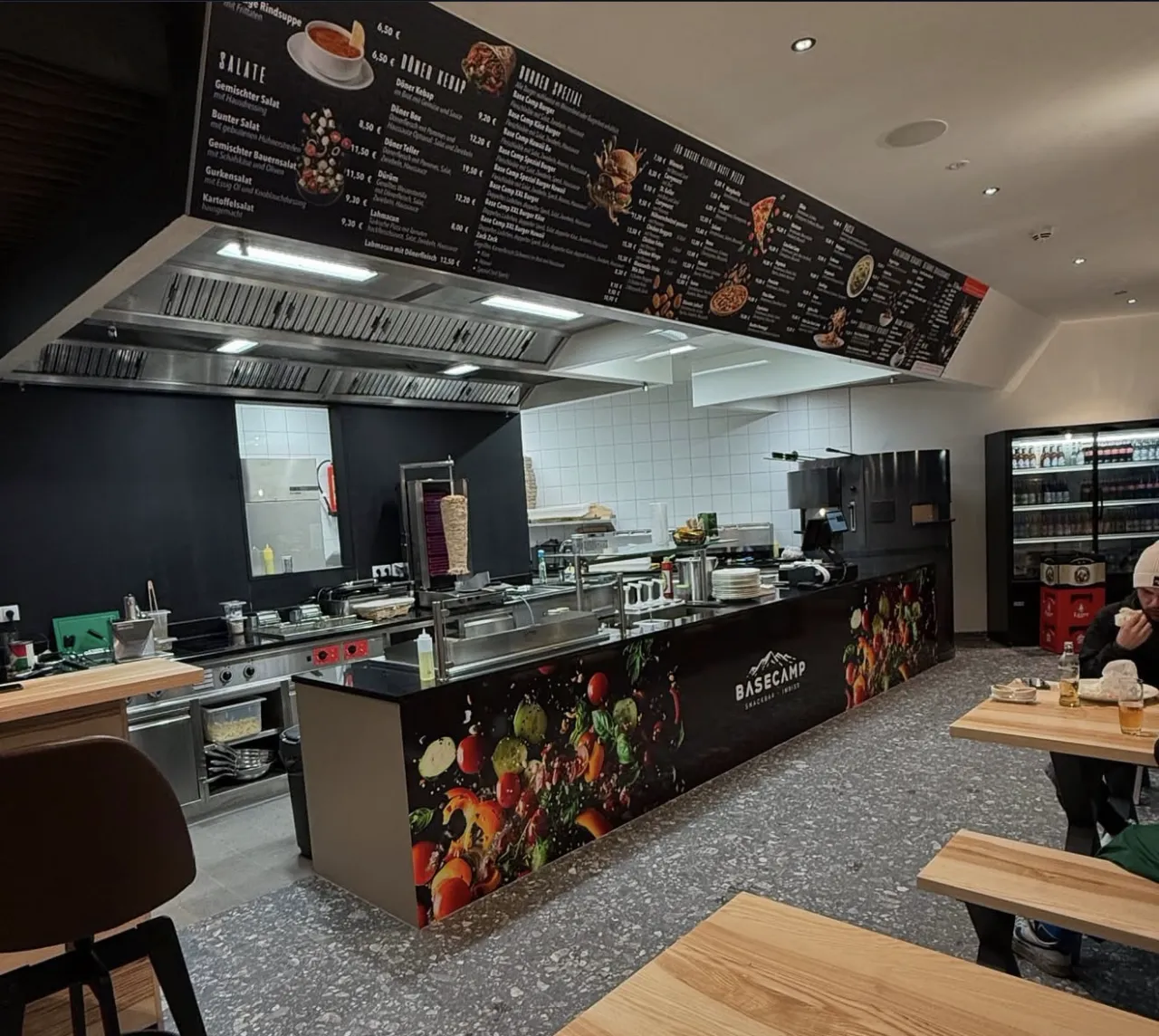 Innenraum der Basecamp Snackbar mit folierter Theke, Zutatenmotiv und beleuchteter Menütafel