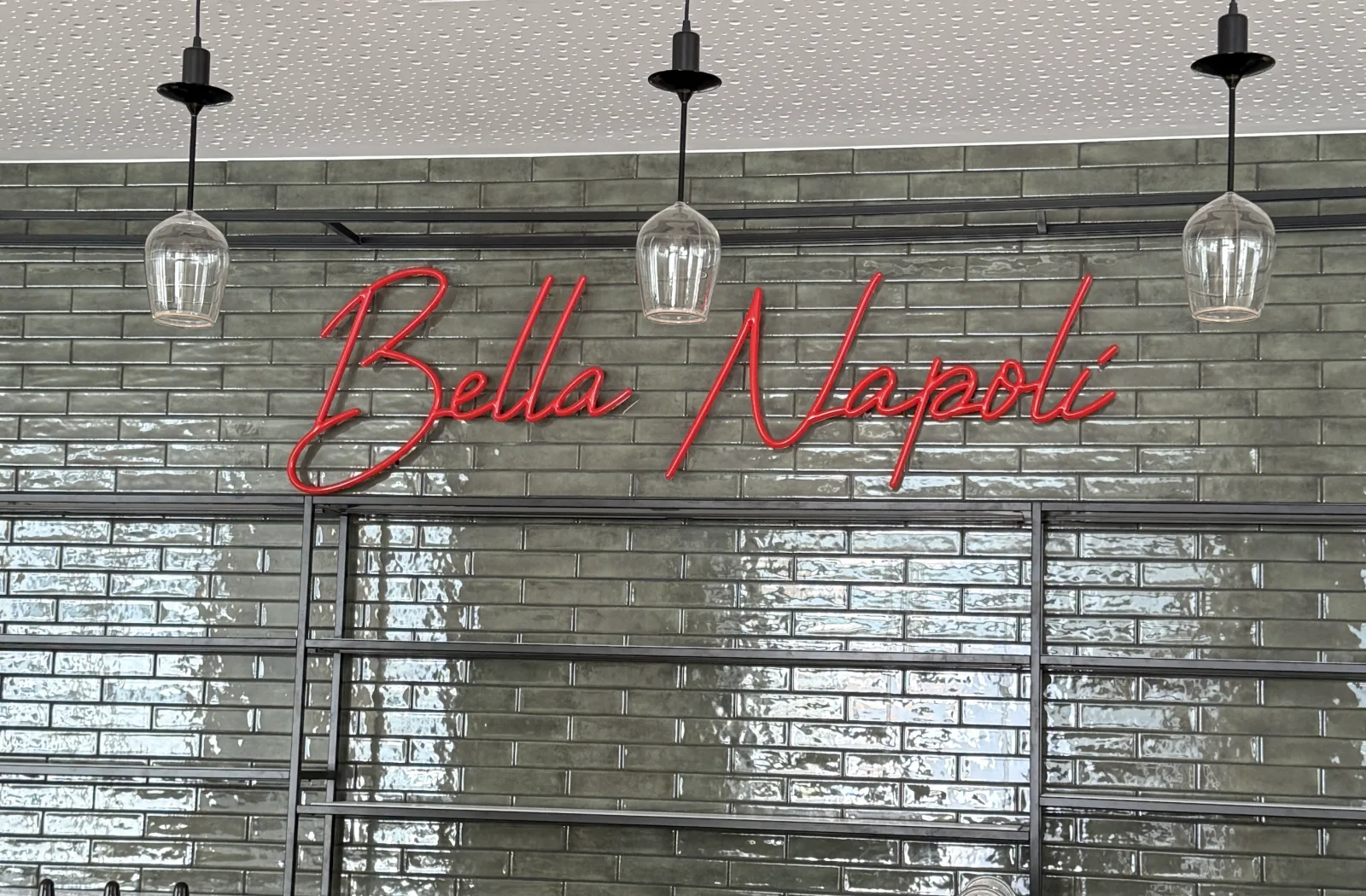 Schriftzug Bella Napoli aus roten LED-Neonröhren auf einer Fliesenwand in Dornbirn, ausgeschaltet bei Tageslicht