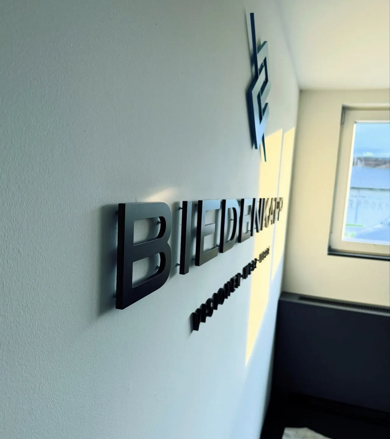 Schwarze 3D-Buchstaben des Biedenkapp-Schriftzugs auf heller Innenwand im Empfang