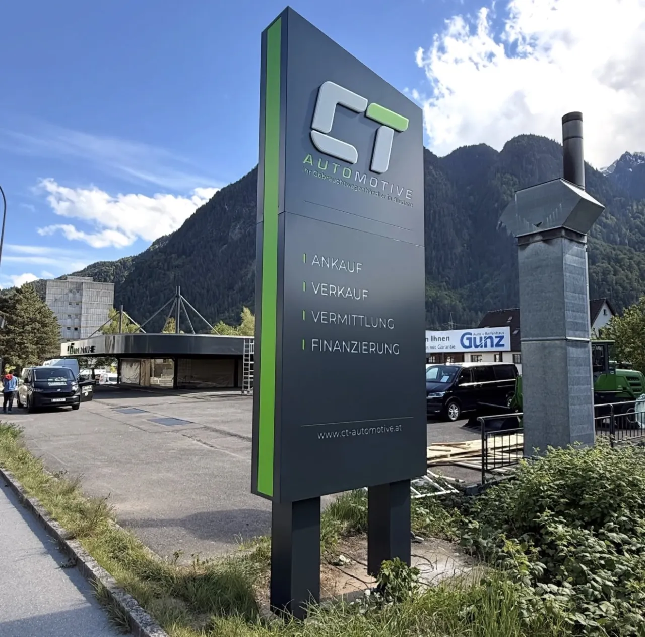 Werbepylon von CT Automotive in Bludenz bei Tageslicht, aus anderer Perspektive vor Bergkulisse