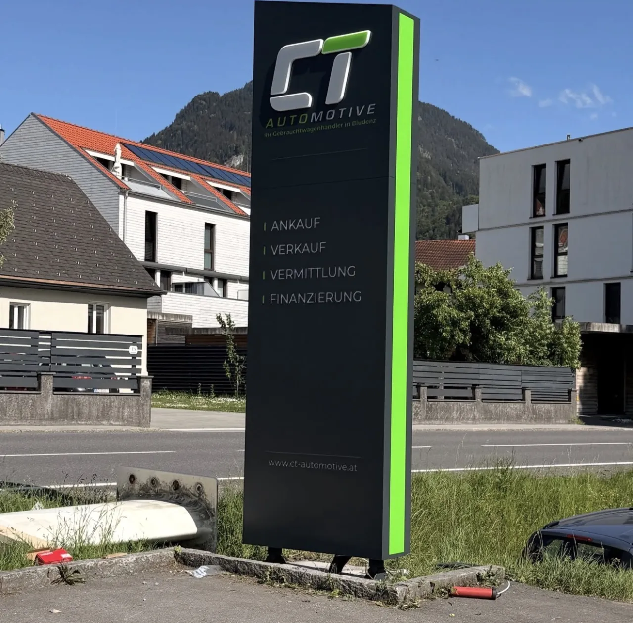Beleuchteter Werbepylon von CT Automotive mit grüner Lichtkante an einer Straße in Bludenz