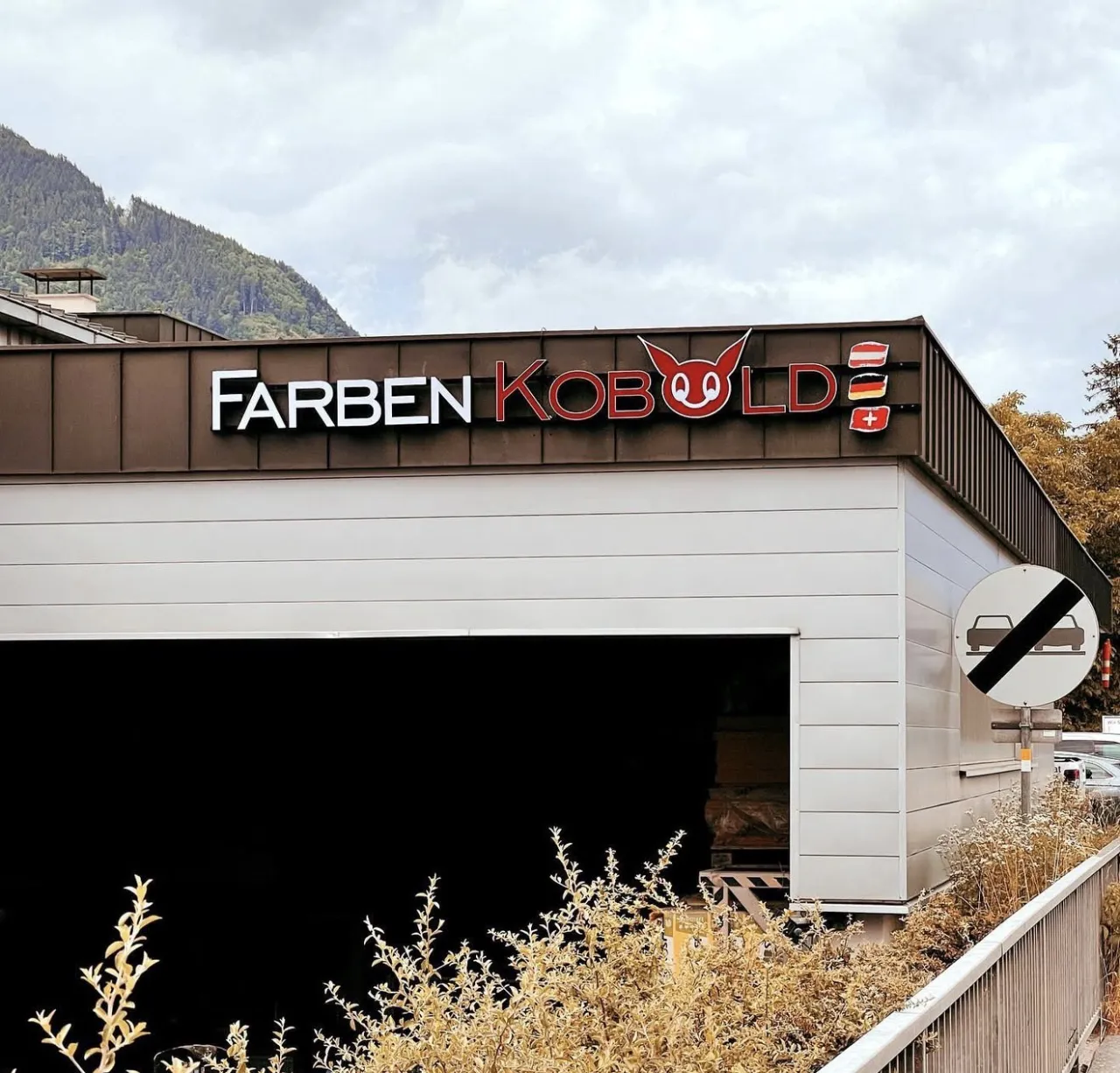 Beleuchteter Schriftzug Farben Kobold mit rotem Kobold-Maskottchen auf dem Dachrand einer Halle
