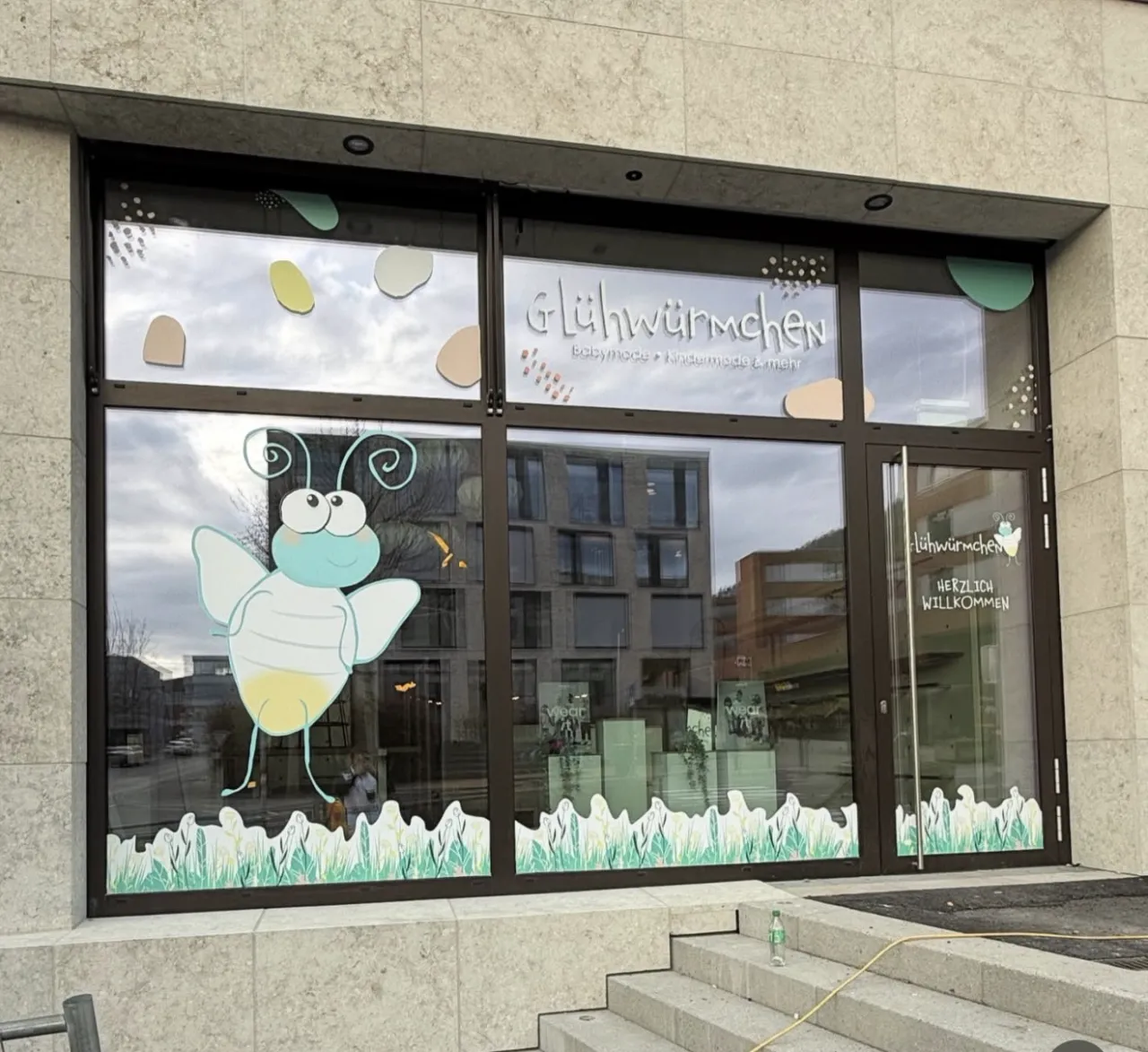Eingangsbereich von Glühwürmchen mit beschrifteter Glastür und Willkommensgruß