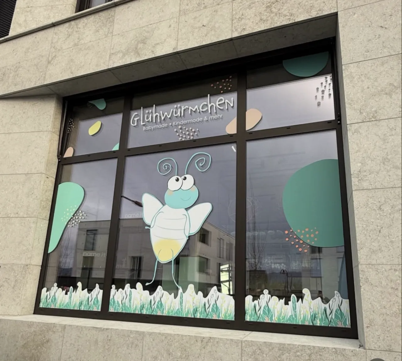 Schaufenster von Glühwürmchen Babymode mit foliertem Glühwürmchen-Motiv, Wiesenband und Schriftzug
