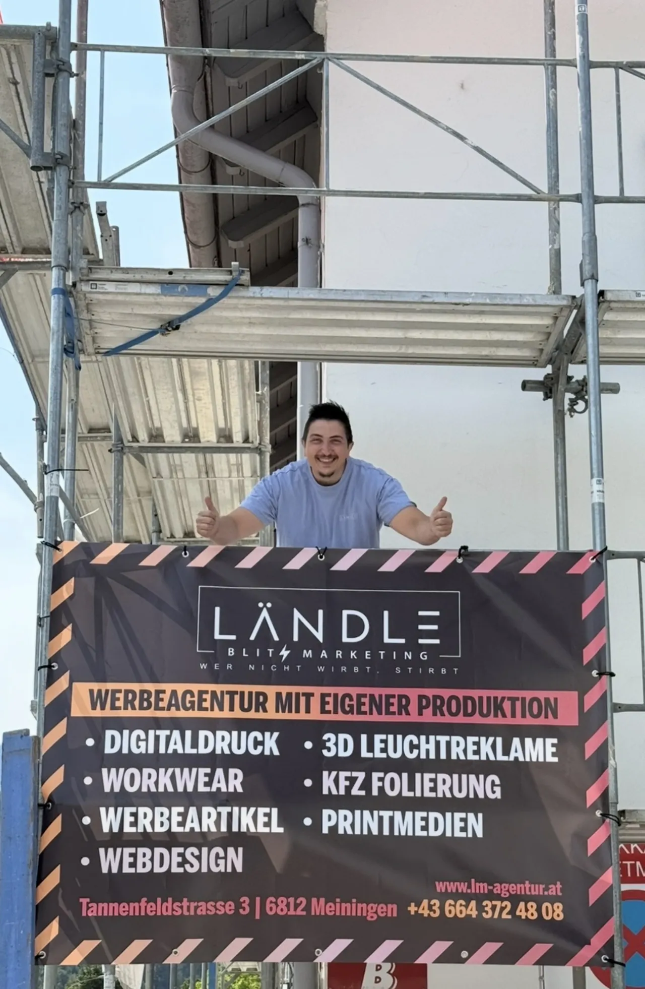 Sait Simsek auf einem Baugerüst über dem Werbebanner von Ländle Blitz Marketing