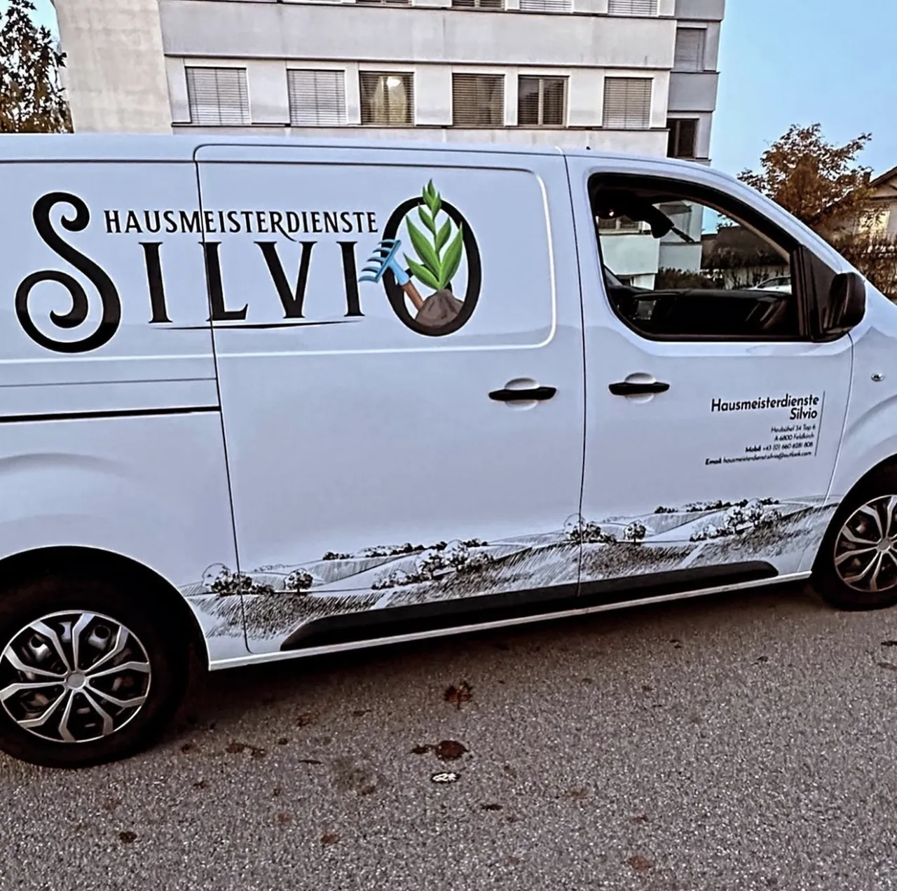 Weißer Transporter mit KFZ-Folierung für Hausmeisterdienste Silvio aus Feldkirch: Logo und gezeichnete Landschaft entlang der Seite